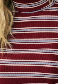 Pull à col roulé côtelé avec des rayures horizontales bordeaux, blanches et bleu clair. Le tissu semble doux avec un ajustement près du cou.