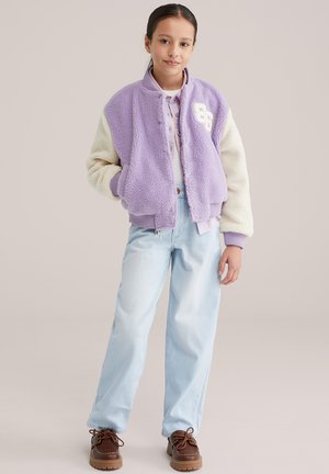 Levendulalila és krémszínű polár bomberdzseki cipzárral elöl, bordázott mandzsettákkal és fehér számfelvarróval. Világoskék farmerral és barna cipővel párosítva.