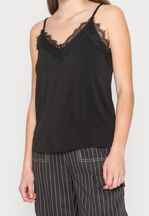 Camisola nera con scollatura a V bordata di pizzo, dotata di sottili spalline e una consistenza liscia e fluida. Abbinata a pantaloni a righe.
