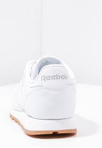 Weiße Reebok-Sneaker mit einem glatten Leder-Obermaterial, besticktem Logo an der Ferse und einer hellbraunen Gummisohle.