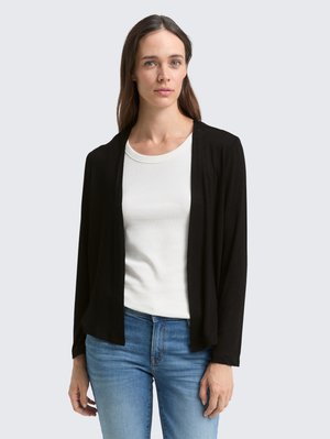 Cardigan léger noir avec un design à l'avant ouvert, doté de manches longues. Associé à un haut blanc à col rond et un jean bleu.