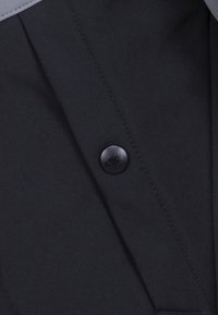 Zwarte button-up shirt met een gladde textuur, met een ronde zwarte knop met een subtiel logo en een schone, op maat gemaakte uitstraling.