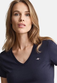 Tricou bleumarin cu decolteu în V, realizat din material moale, cu un mic logo brodat pe pieptul stâng și mâneci scurte.