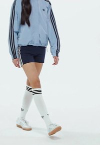 Svetlomodrá bunda na zips s čiernymi pruhmi, námornícke šortky, biele ponožky po kolená s čiernymi pruhmi a biele tenisky s gumenými podrážkami.