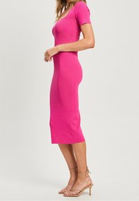 Abito rosa a maglia aderente con maniche corte, scollo rotondo e lunghezza a metà polpaccio; texture liscia con spacchi laterali per facilitare i movimenti.