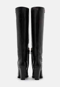 Bottes noires en cuir jusqu'au genou avec un design ajusté, des talons blocs hauts et des zips visibles sur les côtés extérieurs. Texture lisse et brillante.