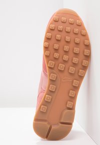 Růžová teniska Nike s texturovaným růžovým svrškem a gumovou podrážkou s kruhovými vzory v kontrastní světle hnědé barvě.