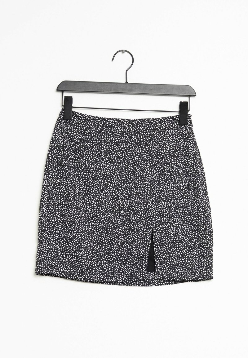 Musta-valkoinen kuviollinen hame, jossa on joustava vyötärö ja etuhalkio, valmistettu kevyestä kankaasta, roikkuu mustassa hangassa.