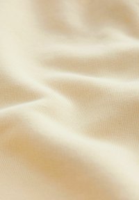 Vaaleanbeige kangas, jossa on sileä ja pehmeä rakenne. Yksityiskohtana hieno poikkiraitakuosi, joka luo hienovaraista syvyyttä ja lämpöä.