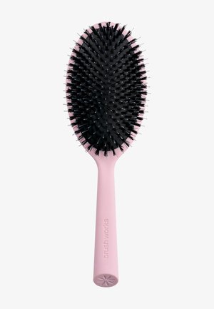 Cepillo de cabello ovalado con cerdas negras y mango rosa claro etiquetado como "brushworks", colocado en posición vertical sobre un fondo blanco.
