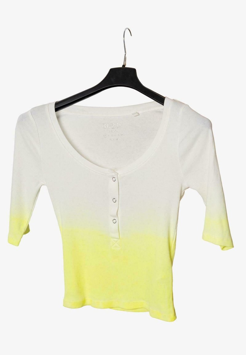 Chemise en maille côtelée blanc à jaune dégradé avec trois boutons sur le devant et manches trois-quarts suspendue sur un cintre noir.