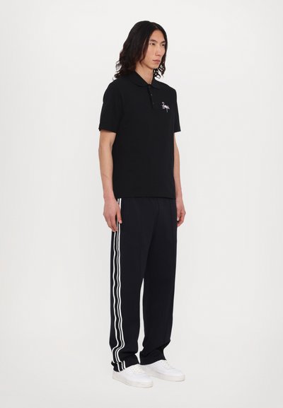 Black polo shirt with short sleeves, featuring a small logo. Paired with black tapered pants with white side stripes and white sneakers.