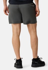 Grå atletiska shorts med en slät yta och justerbar midja, i kombination med svarta snörskor och svarta strumpor.