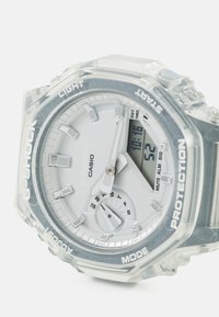 Montre G-Shock transparente avec un cadran rond, un cadran argenté et des accents gris. Comprend des affichages analogiques et numériques, un bracelet en silicone texturé et des marquages audacieux.