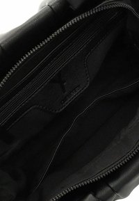 Zwarte leren handtas interieur met zachte textuur, met een ritsvak en compartimentafscheidingen. Minimalistisch ontwerp met logo detail.