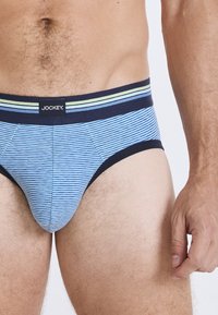 Blå och vita randiga kalsonger med midjeband i marinblått och gröna och marinblå accenter. Tillverkade av bomull, elastisk midja och figurnära design.