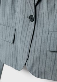 Blazer à fines rayures grises avec un design classique, deux poches avant et une fermeture par un bouton noir unique, fabriqué en tissu texturé.