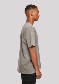 Gray oversized t-shirt with short sleeves and a crew neck, featuring a pink graphic detail on the front and a faded, textured finish.