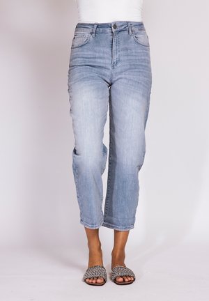 Woman wearing light blue cropped jeans and black-and-white chain-link patterned slip-on sandals.