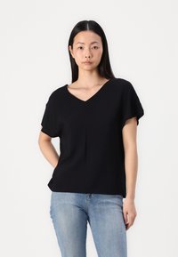 Top negro de cuello en V hecho de tejido suave, con mangas cortas y un corte relajado. Combinado con jeans de un azul claro. Diseño simple y minimalista.