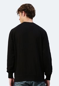 Felpa nera realizzata in tessuto morbido con una vestibilità comoda, caratterizzata da maniche raglan e polsini a coste, indossata da una persona vista da dietro.
