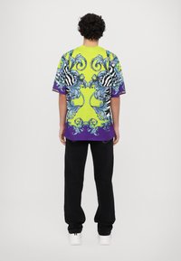 Košile s krátkým rukávem v jasně zelené barvě se spirálovými vzory v modré a černé barvě; fialové akcenty; nošena s černými kalhotami a bílými botami.