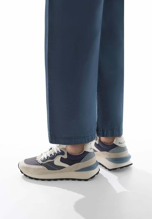 Baskets en daim et maille, arborant un schéma de couleurs bleu, beige et gris, avec une semelle épaisse et un détail de laçage bien en vue.