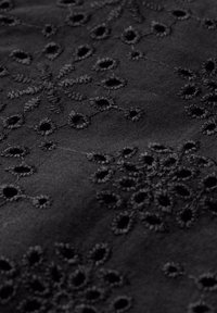 Svart tyg med broderade snöflingemönster, med cirkulära utskärningar och strukturerade stygn. Slät yta och enhetlig färg.