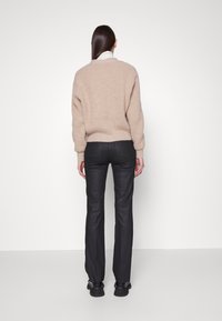 Beige stickad tröja med en ribbad textur, avslappnad passform och sänkt axlar, kombinerad med svarta slim-fit byxor och svarta skor.