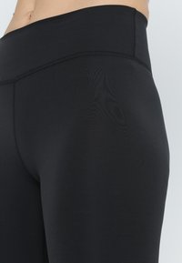 Leggings neri a vita alta realizzati in tessuto liscio ed elastico con cuciture piatte. Presentano una vita ampia per il massimo comfort e una silhouette aderente.