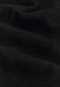 Gros plan sur un tissu noir avec une fine texture côtelée et des plis doux créant de douces ondulations.