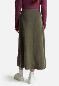 Sukně olivově zelené barvy, střední délky, z texturované látky s vysokým pasem. S kombinací bílých tenisek a bílých ponožek, viděno zezadu.