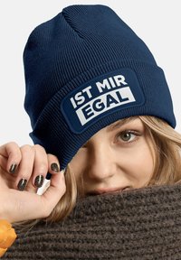 Navy beanie made of ribbed knit fabric featuring a rectangular white patch with the text "IST MIR EGAL." Soft texture, snug fit.