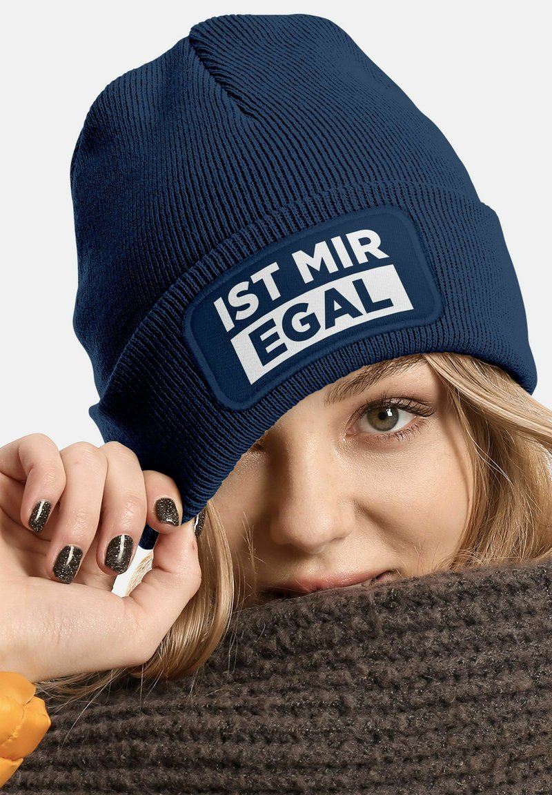 Navy beanie made of ribbed knit fabric featuring a rectangular white patch with the text "IST MIR EGAL." Soft texture, snug fit.