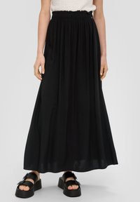 Zwarte maxi rok met een geplooide elastische tailleband, vloeiende stof en een zachte textuur. Gecombineerd met chunky zwarte sandalen met gespaccenten.