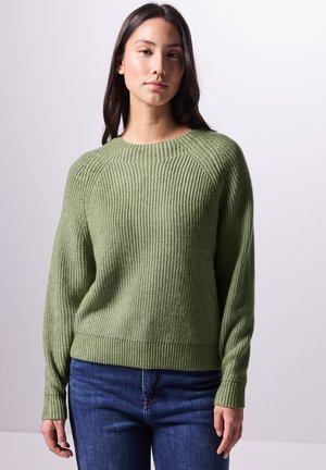 Groene geribbelde gebreide trui met een ronde hals en verlaagde schouders, voorzien van lange mouwen en een aansluitende zoom, gecombineerd met blauwe jeans.