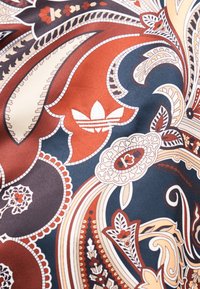 Motif complexe de tissu avec des formes cachemire en rouille, marine, crème et noir, présentant le logo blanc trefoil d'Adidas au centre.