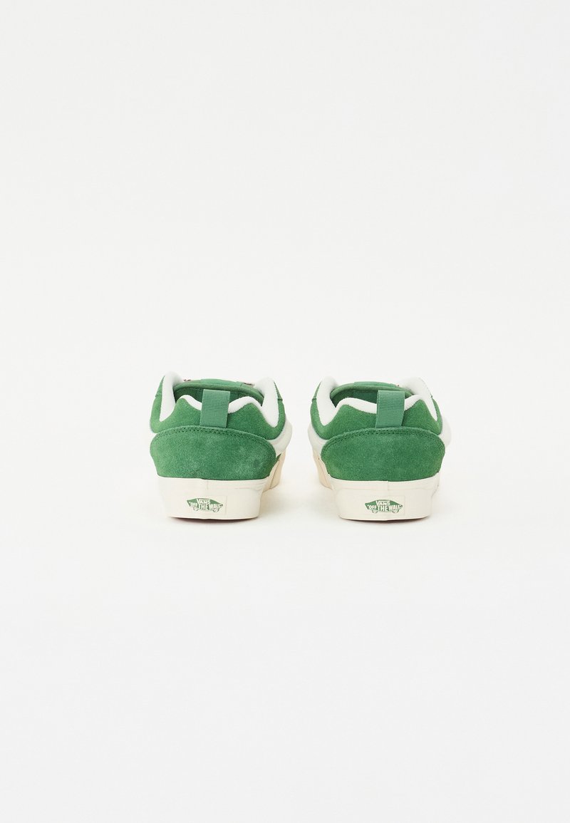 Des baskets en daim vert avec un col et une languette rembourrés en blanc, et une semelle en caoutchouc beige. L'arrière présente un détail de logo près du talon.