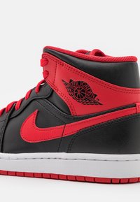 Basket montante Air Jordan noire et rouge montrant le logo latéral, le swoosh Nike rouge, les lacets rouges et la semelle blanche.