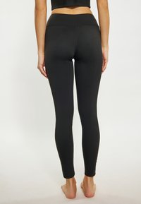 Fekete leggings magas derekú, rugalmas anyagból készült. Simaszerkezetű, látható minták vagy díszítések nélkül. Rásimuló fazon.