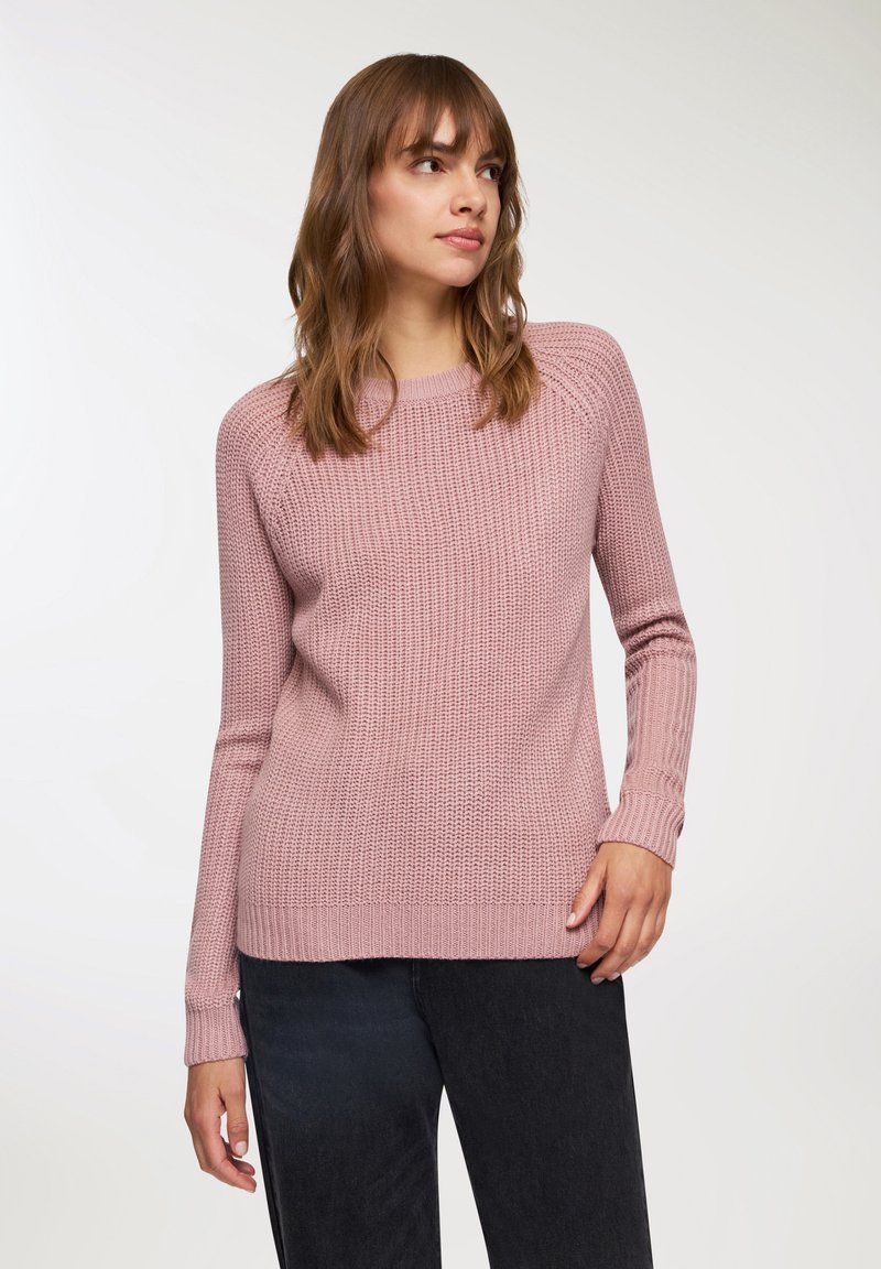 Jasnoróżowy sweter z dzianiny o żebrowanej fakturze, z długimi rękawami i okrągłym dekoltem, w zestawieniu z ciemnymi dżinsami. Prosty i uniwersalny design.