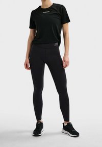 Černé sportovní tričko s logem na hrudi, v kombinaci s černými legínami s logem na pase. Nosí se s černobílými teniskami.