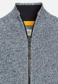 Jacke mit Reißverschluss aus strukturiertem grauem Strickstoff, mit einem schwarzen gerippten Kragen und gelbem Akzent am Hals, mit einem teilweisen Reißverschluss.
