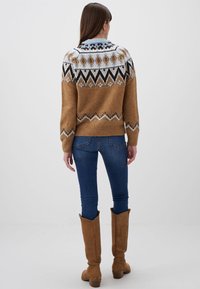 Maglione di lana marrone con un collo decorato in blu, nero e bianco. Abbinato a jeans di denim blu e stivali al ginocchio color cammello.
