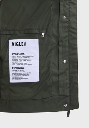 Olive green jacket interior features a white label with text. Material appears smooth, with a matte finish and subtle stitching detailing.