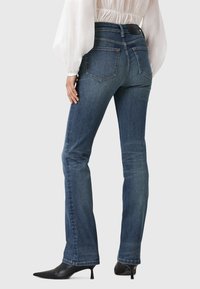 Donkerblauwe jeans met een slim fit, vijf zakken en een subtiele vervaging. Beschikt over een hoge taille en een zoom die iets uitloopt aan de onderkant.