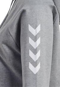Gros plan sur une manche de sweat-shirt gris avec quatre flèches chevrons blanches pointant vers le bas imprimées en rangée verticale.