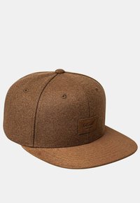 Brown snapback cap made from textured fabric, featuring a flat brim, rounded top, and a square patch with brand logo on the front.