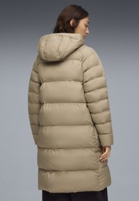 Cappotto puffer beige con cappuccio, caratterizzato da un design trapuntato e un taglio di lunghezza media. Texture liscia e lucida con silhouette dritta.