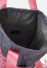 Harmaa kangaskassi naruilla, joissa on vaaleanpunaiset hihnat. Sisätiloissa on vetoketjullinen tasku ja sileä, vuorattu pinta. Brändilippu näkyvissä.